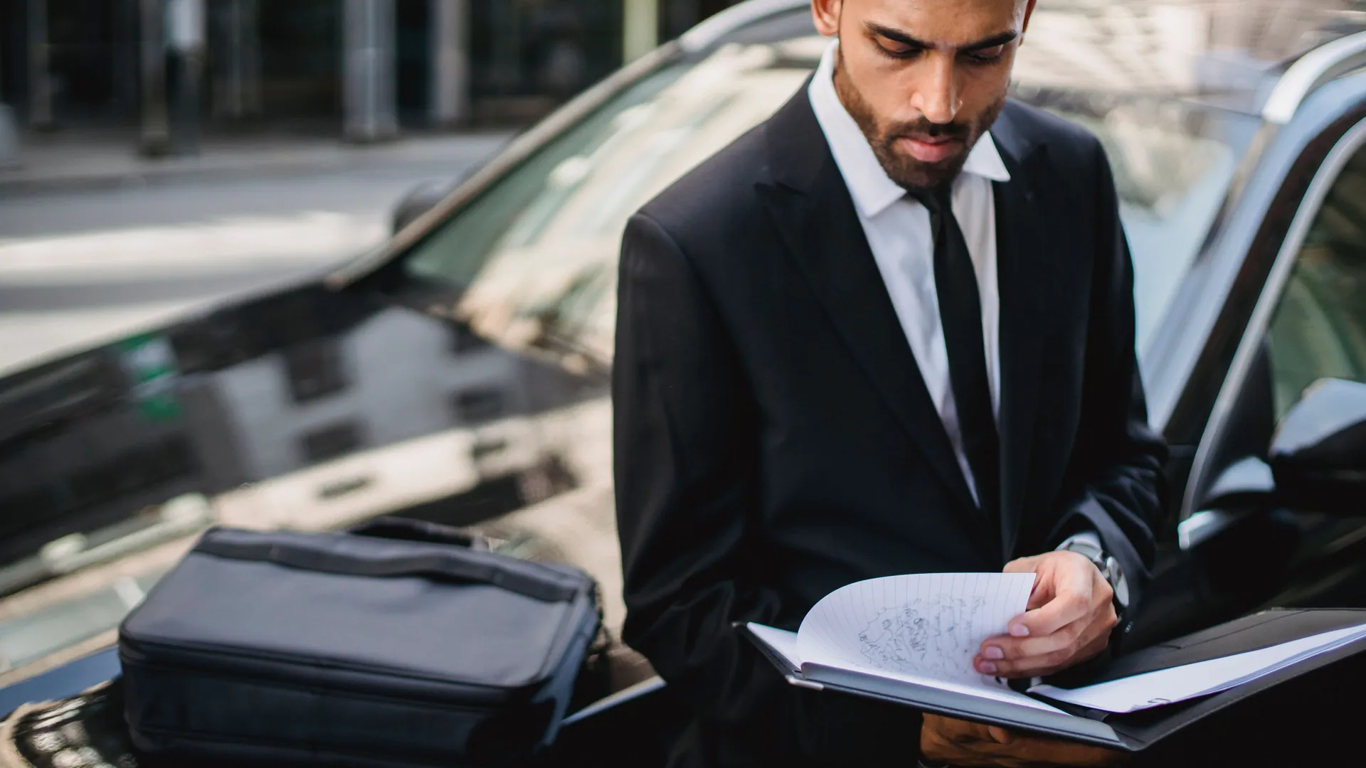 Chauffeur VTC en costume consultant son carnet devant sa berline